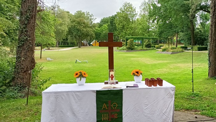 Gedenktisch im Freien mit Kerzen, Kreuz und religiösen Symbolen in einem parkähnlichen Friedhof.