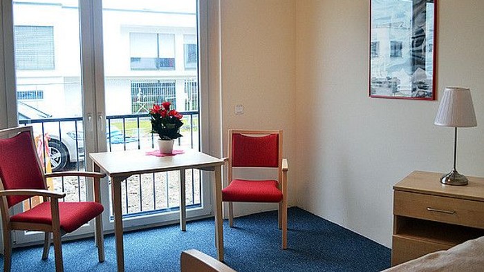 Gemütliches Zimmer mit roten Stühlen, kleinem Tisch, Balkonblick und moderner Einrichtung.