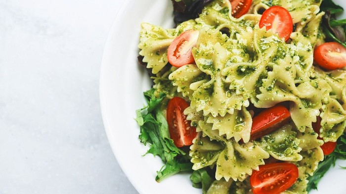 Pasta salad with pesto, tomatoes, and greens on a white plate