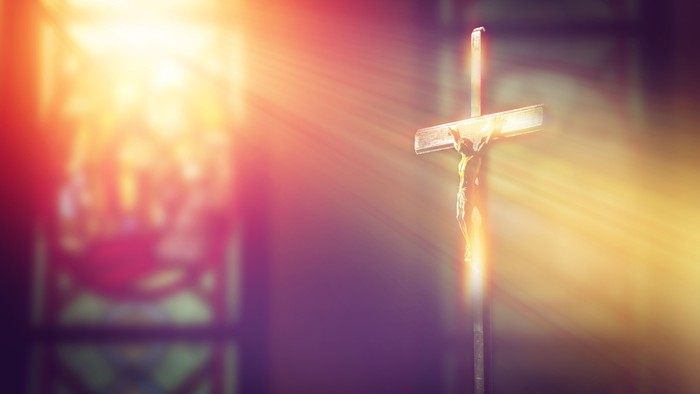 A crucifix stands prominently in a church, illuminated by stained glass light.