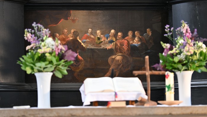 Religiöser Altar mit einem Gemälde des Letzten Abendmahls, flankiert von Blumengestecken und liturgischen Gegenständen.