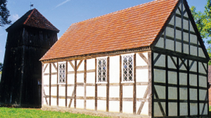 Das Bild zeigt ein traditionelles Fachwerkhaus mit rotem Dach auf einem grasbewachsenen Grundstück.