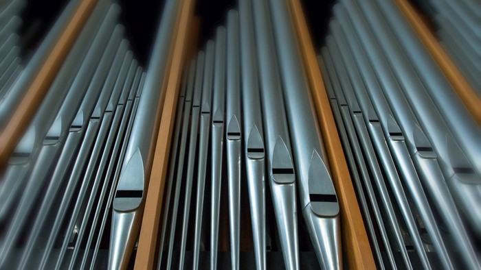 Nahaufnahme polierter Metallpfeifen einer großen Orgel, in parallelen Reihen angeordnet.