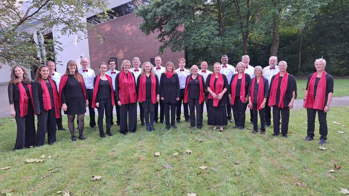 Eine Gruppe von Menschen in passenden roten Schals und schwarzer Kleidung posiert gemeinsam im Freien für ein Gruppenfoto.