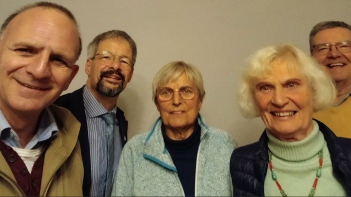 Fünf Personen, die fröhlich zusammen in einem eng verbundenen Gruppenfoto lächeln.