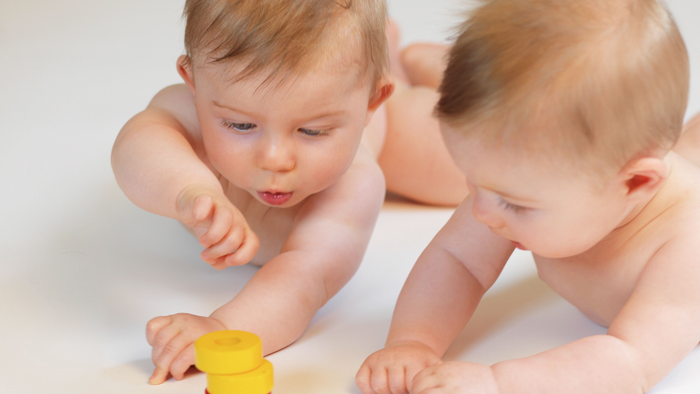 Zwei Babys spielen mit bunten Stapeltürmen auf einer hellen Oberfläche.