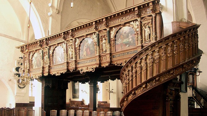 Prächtige, verzierte Holztreppe in einem großen, hellen Raum mit hohen Decken und Kronleuchtern.
