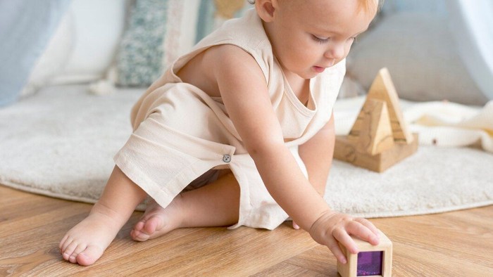 Baby spielt mit Holzklotz auf dem Boden.