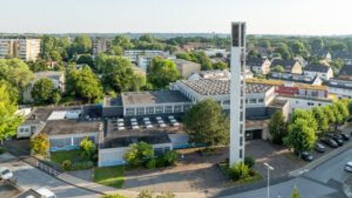 Städtisches Gebiet mit Industriegebäuden, hohem Schornstein und umliegenden Wohnhäusern mit grünen Bäumen.