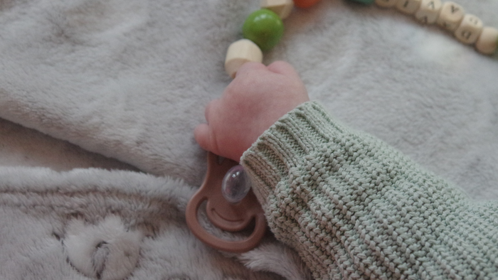 Ein Kinderhand mit einem Perlenarmband und einem hellgrünen gestrickten Bündchen auf einer weichen Decke.