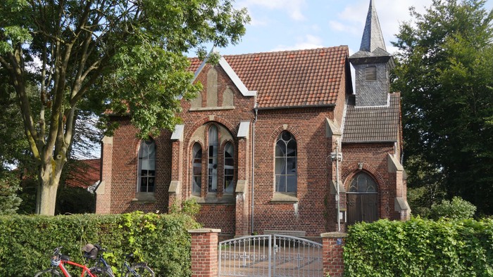 Kirchengebäude aus Ziegeln mit spitzem Turm und weißem Zaun