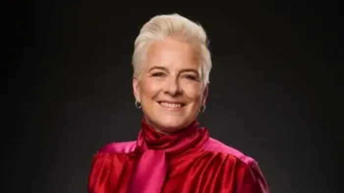 En smilende kvinde i en livlig pink satinjakke poser selvsikkert mod en mørk baggrund.