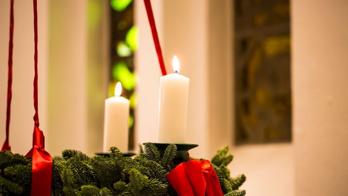 Tre tændte stearinlys på en grøn krans med røde bånd.