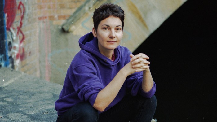 Eine Person in einem lila Kapuzenpulli sitzt auf Stufen neben einer bunten, mit Graffiti bedeckten Backsteinmauer.