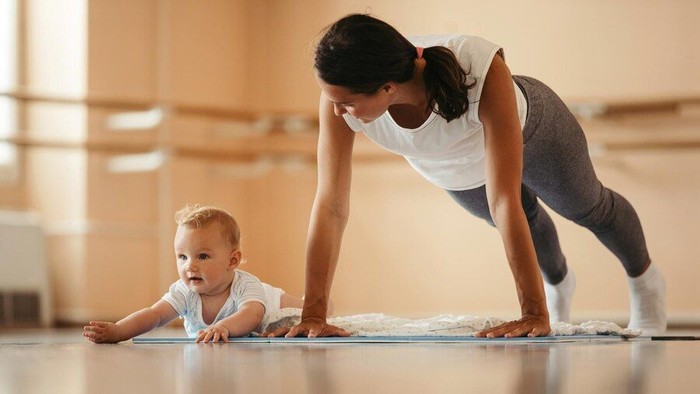 Eine Frau macht mit ihrem Baby Yoga auf einer Matte.