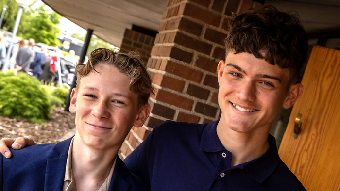 To smilende unge mænd i blå skjorter med en tekst, der opfordrer til genbrug af konfirmationstøj til fester.