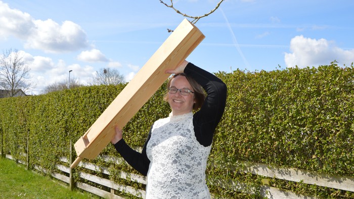 Kvinde holder et stykke træ op i en have.