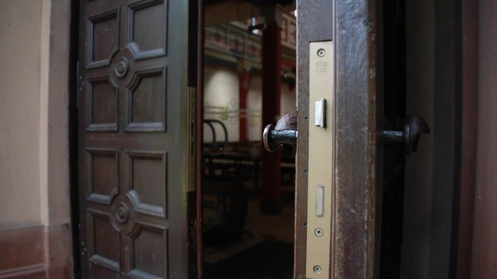 Eine teilweise geöffnete Holztür mit einem Messingschloss und dekorativer Verkleidung gibt den Blick auf einen inneren Flur frei.