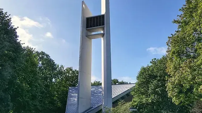 Modernes Architekturdenkmal mit hohen, schlanken vertikalen Säulen und einer offenen, erhöhten Plattform in einer Parkanlage.