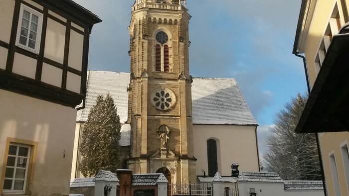 Gotischer Kirchturm mit Uhr und Kreuzigungsgruppe vor historischem Hintergrund