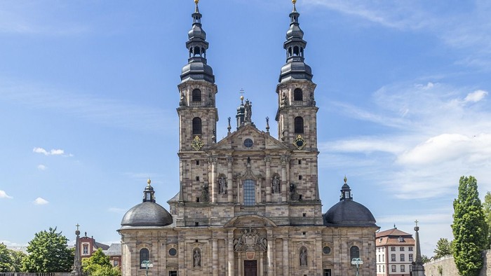 Historische Kirche mit Zwillingstürmen und Kuppeln vor blauem Himmel.