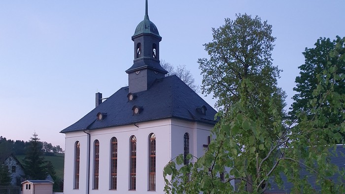 Kirche mit Friedhof und Bäumen im Hintergrund