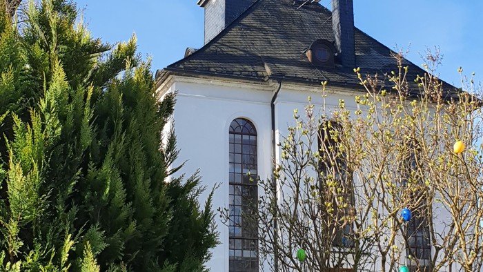 Weiße Kirche mit grünem Turm und goldener Spitze, umgeben von Bäumen und Büschen