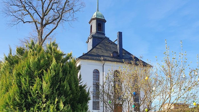 Weißes Kirchgebäude mit blauen Dächern und grünem Garten