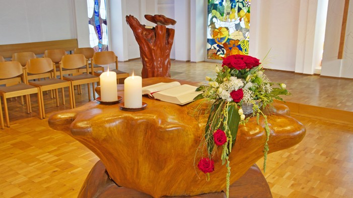Holztisch mit Kerzen und Blumen, Stühlen und Gemälde im Hintergrund.