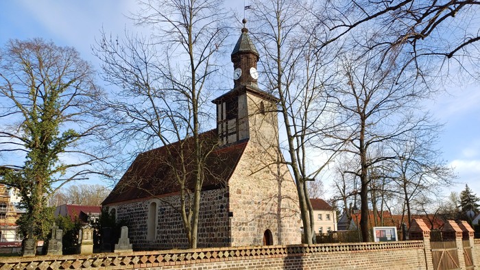 Alte Kirche mit Turm und Mauer, umgeben von kahlen Bäumen