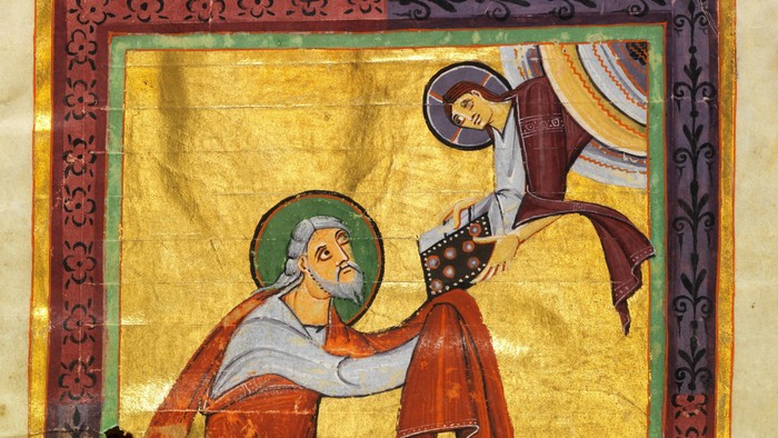 Mittelalterliches illuminiertes Manuskript, das einen bärtigen Heiligen mit einem Buch zeigt, während eine engelhafte Gestalt von oben herabsteigt.