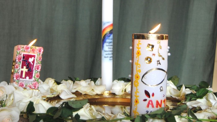 Drei brennende Kerzen auf Holzdekoration mit Blumen und grünem Hintergrund