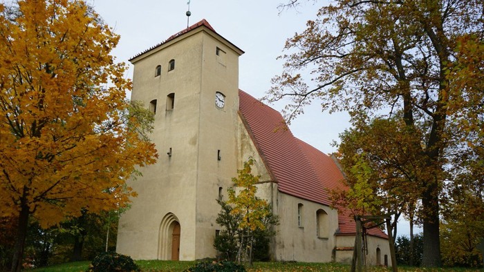 Kirche mit quadratischem Turm und rotem Satteldach, umgeben von herbstlich gefärbten Bäumen.