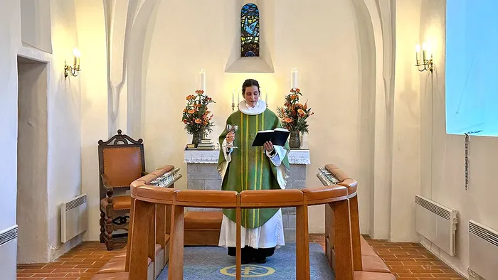 Præsten afholder en gudstjeneste ved et alter pyntet med lys og blomster i et roligt kapel.