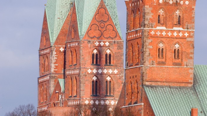 Zwei hohe Backsteintürme mit spitzen grünen Dächern vor blauem Himmel