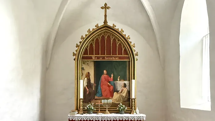 Religiøs alterniske med et malet motiv af Kristus med disciple og tændte lys på et hvidt bord.
