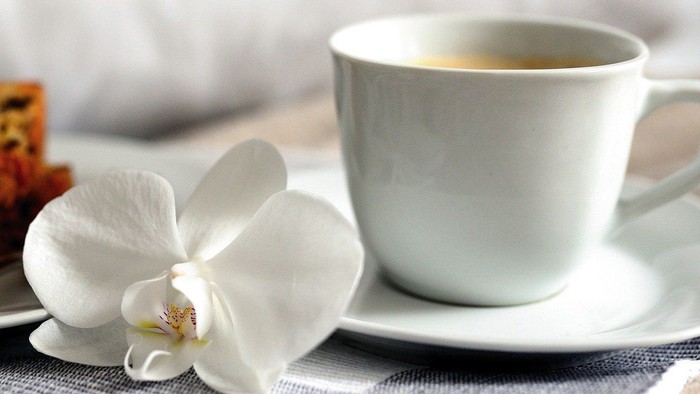 Ein Stück Kuchen, eine Tasse Kaffee und eine Orchidee auf einem Tisch