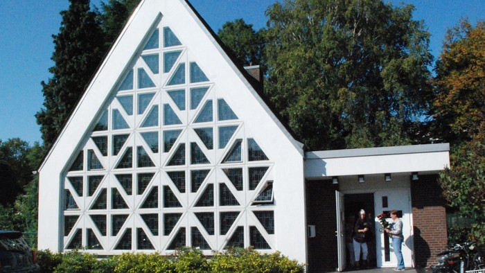 Weißes Gebäude mit geometrischen Fenstern und Menschen am Eingang