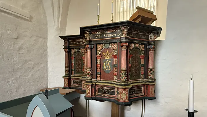 Indviklet prædikestol med farverige udskæringer og latinske indskrifter inde i en kirke.