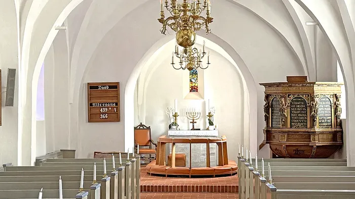 Elegant synagogeinteriør med en træark, lysekrone og pænt arrangerede træbænke.