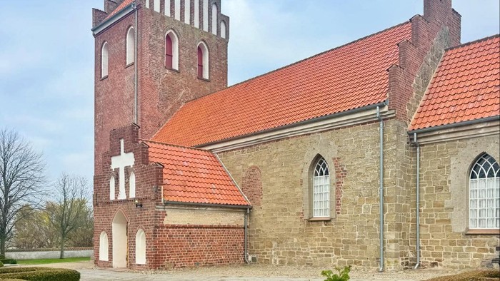 Historisk stenkirke med rødt tag og højt tårn.