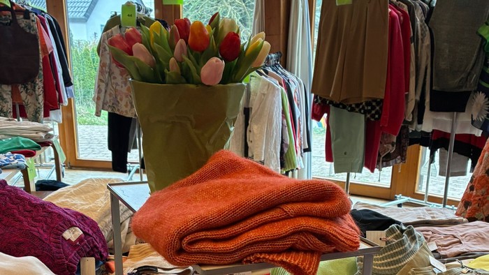 Bunte gefaltete Kleidung und Schals, ausgestellt in einem gemütlichen Modegeschäft mit floralen Tischdekorationen.