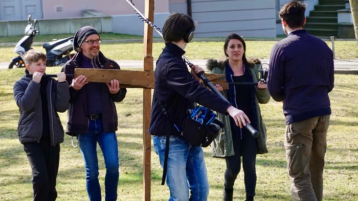 Eine Gruppe hebt gemeinsam einen Holzbalken im Freien an und scheint etwas zusammenzubauen.