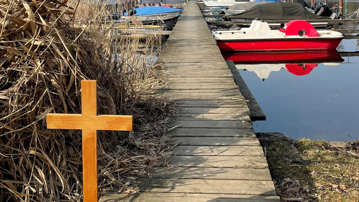 Foto vom Bootssteg mit Kreuz im Vordergrund und Boot im Hintergrund