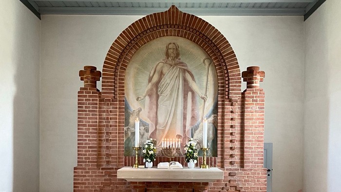 Religiøst alterområde med en statue af Kristus og en halvcirkelformet grøn bænkarrangement.