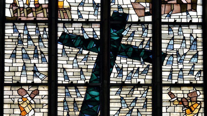 Das Bild zeigt ein buntes Kirchenfenster mit Kreuz und Figuren