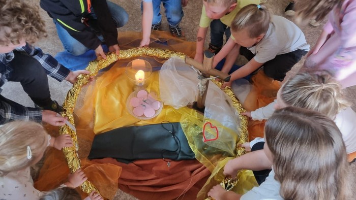 Kinder versammeln sich um einen geschmückten Korb mit einer Kerze und nehmen an einer Gruppenaktivität oder einem Ritual teil.