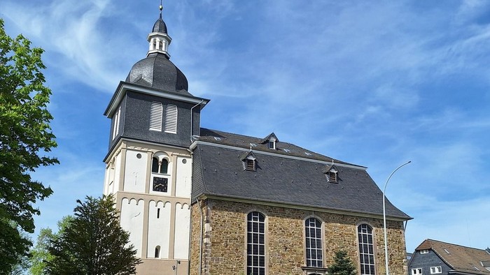 Historische Kirche mit hohem Turm und steinerner Fassade vor klarem blauem Himmel.