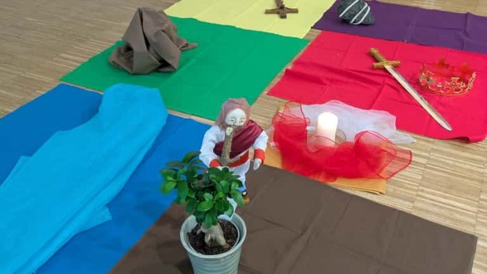 Bunte Stoffquadrate auf dem Boden arrangiert, mit einer kleinen Topfpflanze und dekorativen Gegenständen.