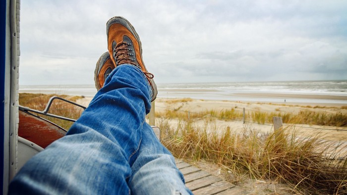 Entspannte Beine auf einem Holzsteg mit Blick auf eine ruhige, windgepeitschte Küstenlandschaft.